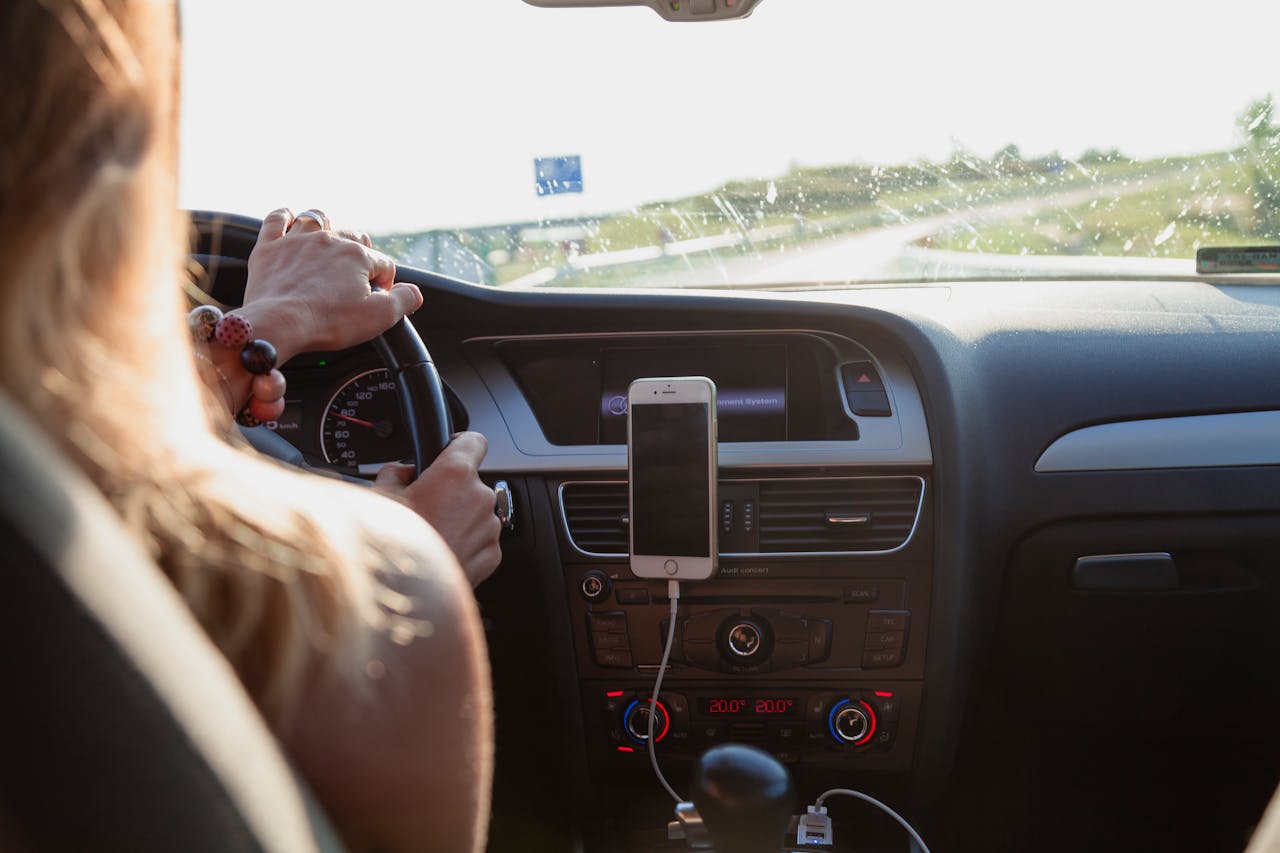 Home View from behind a woman driving a car on a sunny day with a phone mounted on the dashboard.